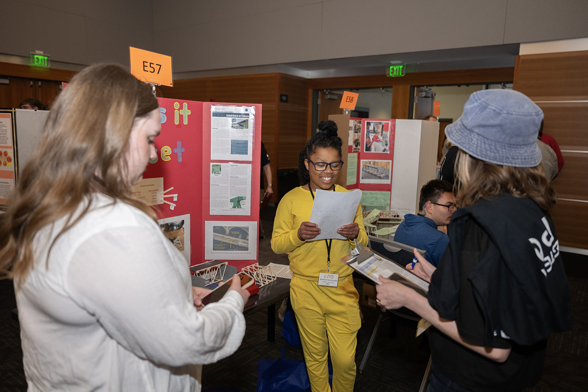 Jamesina Hammonds, center, an Oakland High School student, describes her research to a judge during the recent RCS STEM Fair, held in the Student Union Ballroom at Middle Tennessee State University in Murfreesboro, Tenn. Hammonds was among 400 students from 19 schools presenting their science, technology, engineering and math research at the sixth annual event on Thursday, March 14. (MTSU photo by James Cessna)