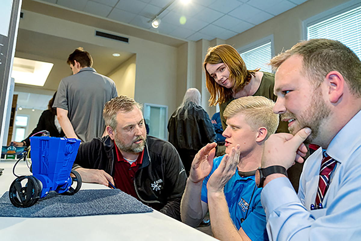 MTSU Engineering Technology Open House senior projects judge Jeff Buck, kneeling left, of Automation Nth listens to Elijah Little, center, Sean Daily and Kelly Maynard, rear, talk about the CL4P-TP self-balancing robot on wheels and how it operates. 