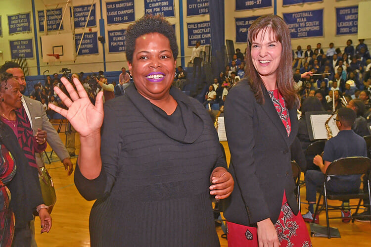 MTSU alumna Erica Stephens (Class of ’02) waves to the crowd after the surprise Oct. 25 announcement at an all-school assembly that she was a winner of the prestigious Milken Educator Award, a national honor that comes with a $25,000 financial prize. Stephens is a fourth-grade math teacher at John P. Freeman Optional School in Memphis, Tenn. At right is Tennessee Education Commissioner Candice McQueen. (Photo courtesy of the Milken Family Foundation)