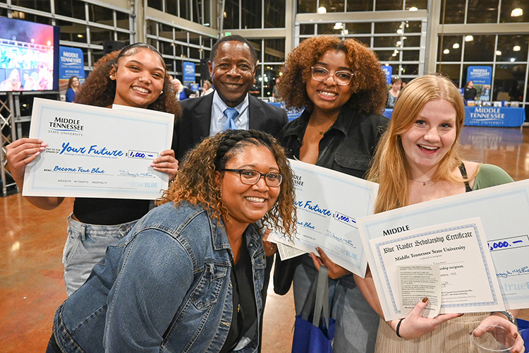 Best friends Aniah Kidd, far left, Zaniyah Williams, second from right, and Jaden Rakestraw, far right, were among the lucky winners in the scholarship drawings at Middle Tennessee State University’s True Blue Tour recruitment stop for prospective students at the Wilma Rudolph Event Center in Clarksville, Tenn., on Thursday, Sept. 28, 2023. The two friends and another scholarship recipient pose with Kidd’s mother, bottom left, and university President Sidney A. McPhee, second from left. (MTSU photo by Stephanie Wagner)