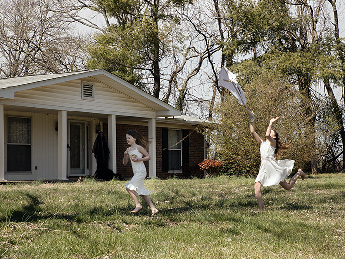 Two children play with a kite in the yard of a brick home as a veiled figure watches from the porch in this untitled photo from "Creation — Adam & Eve" by MTSU adjunct professor and photography alumnus Chuck Arlund, on display as part of the “2022 MTSU Photography Faculty Exhibition” through Friday, April 15, at the university’s famed Baldwin Photographic Gallery in the College of Media and Entertainment. (photo courtesy of Chuck Arlund)