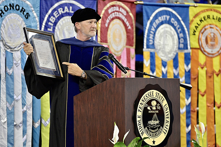 MTSU human sciences professor Rick Cottle, 2020-21 president of the university's Faculty Senate, holds his framed rejection letter from Auburn University, where he later earned undergraduate and doctoral degrees, while encouraging students to "show up and do the work" at MTSU's summer 2021 commencement ceremony Saturday, Aug. 7, in Murphy Center. MTSU presented degrees to 825 new graduates of the August Class of 2021 at the event. (MTSU photo by Andy Heidt)